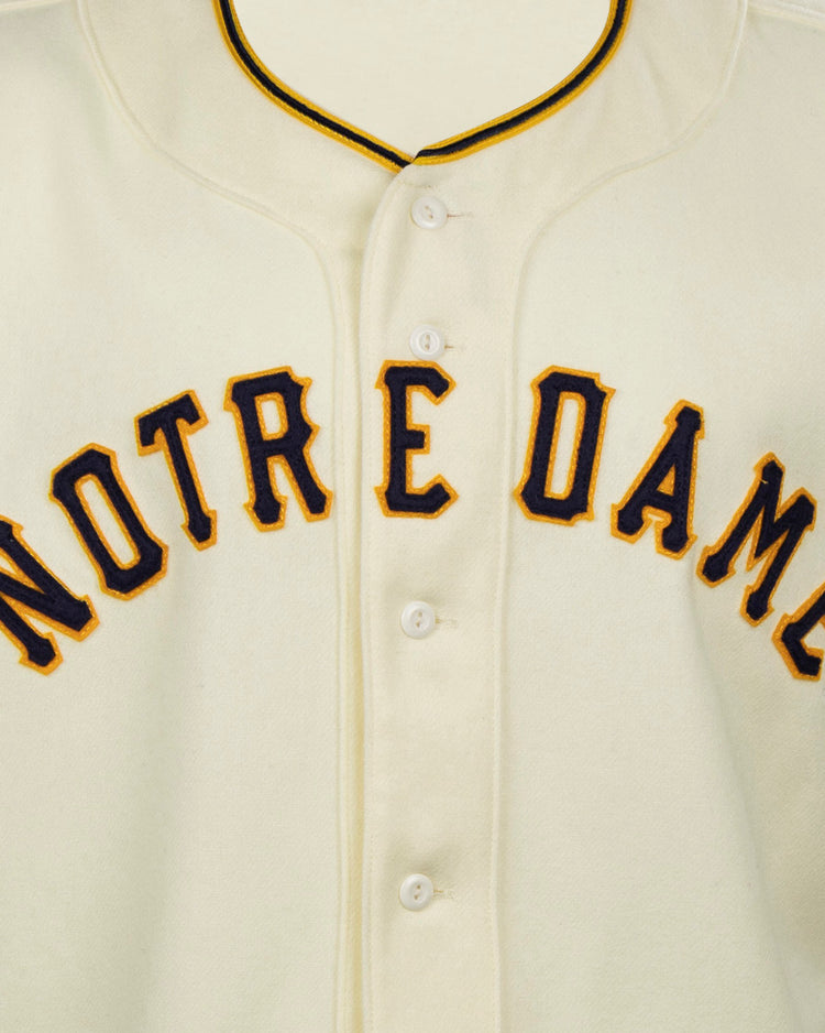 The EFF University of Notre Dame 1956 Home Jersey is an authentic cream flannel with NOTRE DAME in bold navy and gold lettering, white buttons, and black-and-gold collar trim, reflecting the classic 1956 baseball style.