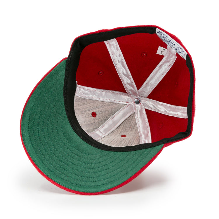 The image shows the inside of an Ebbets Field Flannels University of Nebraska 1958 Vintage Ballcap, featuring a red exterior, green underbrim, white lining, visible stitching, and a size tag on the sweatband.