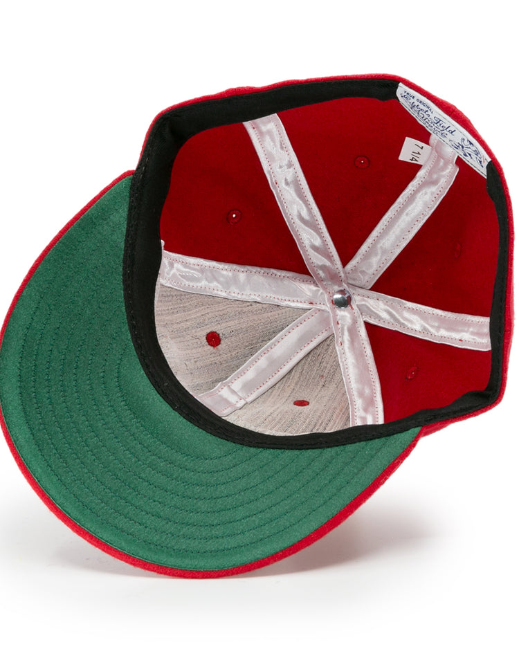 The image shows the inside of an Ebbets Field Flannels University of Nebraska 1958 Vintage Ballcap, featuring a red exterior, green underbrim, white lining, visible stitching, and a size tag on the sweatband.
