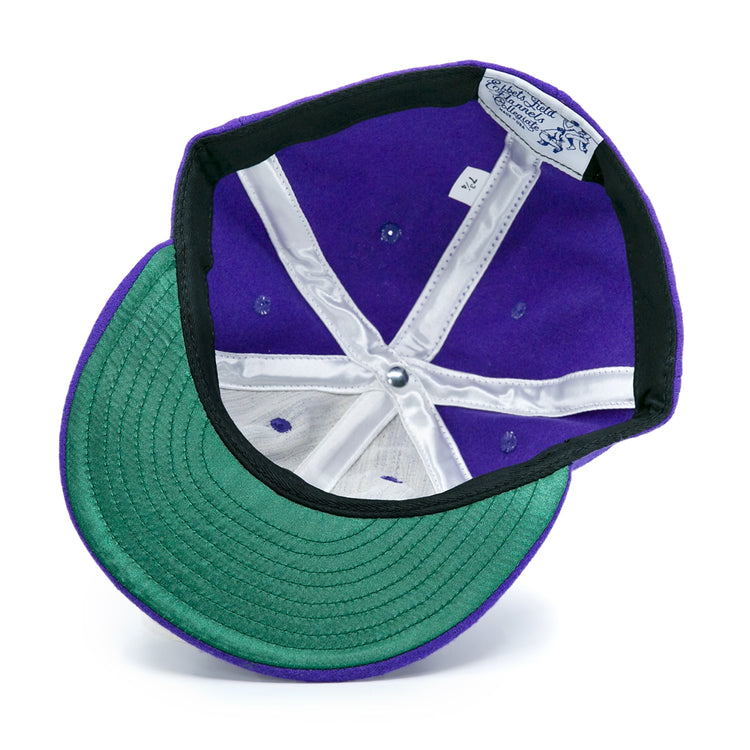 The EFF Northwestern University 1961 Vintage Ballcap, shown upside down on a white background, displays its purple wool fabric, green under-brim, white stitching, and inner band tags.