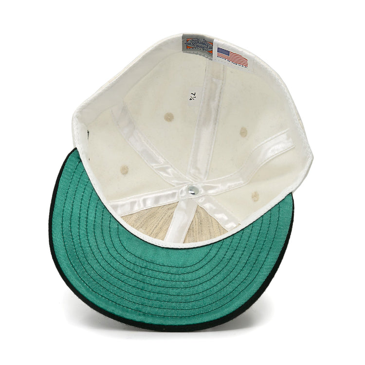An inside view of the EFF New York Knickerbockers Vintage Inspired Ballcap reveals a white crown, green underbrim with black edge, size tag 7 1/4, and a small American flag tag on the inner lining of this genuine wool cap.