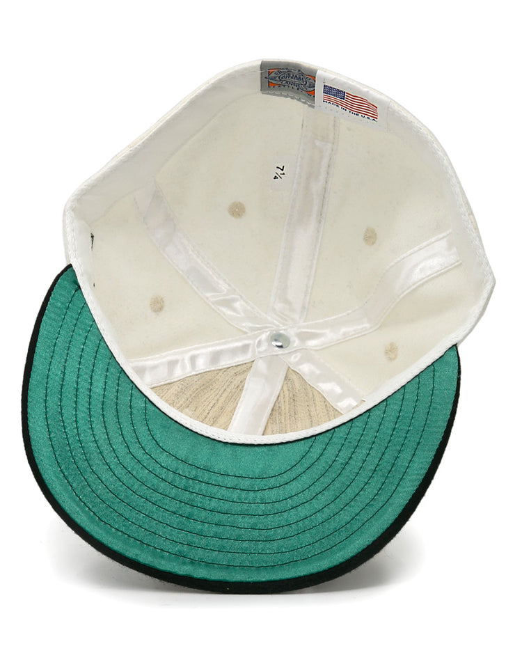An inside view of the EFF New York Knickerbockers Vintage Inspired Ballcap reveals a white crown, green underbrim with black edge, size tag 7 1/4, and a small American flag tag on the inner lining of this genuine wool cap.
