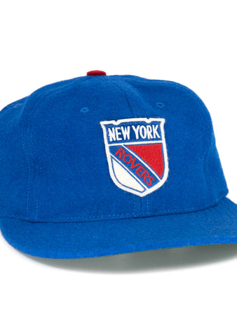 The EFF New York Rovers Vintage Ballcap is a blue hand-sewn wool cap with a front shield logo, side EHL patch, red top button, flat brim, and retro hockey style.