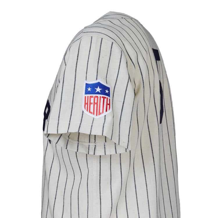 Side view of a white pinstriped EFF New York Black Yankees 1942 Home Jersey sleeve with a red, white, and blue HEALTH patch and stars. The number 9 is partially visible on the back.