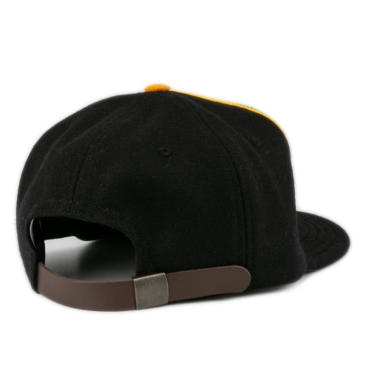 The Oakland Caskets Co. 1938 Vintage Ballcap by EFF is shown from the back, displaying a brown adjustable strap with metallic clasp. The curved brim and yellow crown accent are partially visible. Made in USA for lasting quality.