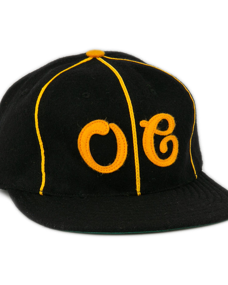 The EFF Oakland Caskets Co. 1938 Vintage Ballcap is a black cap with yellow piping, bold OC front stitching, a yellow top button, and flat brim. Made in the USA for classic style and quality.