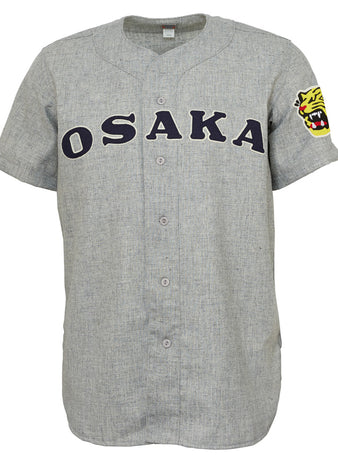 The EFF Osaka Tigers 1959 Road Jersey is a gray Japanese baseball jersey with OSAKA in bold black letters across the chest, a yellow tiger head patch on the left sleeve, button front, and short sleeves—classic Tigers inspiration.
