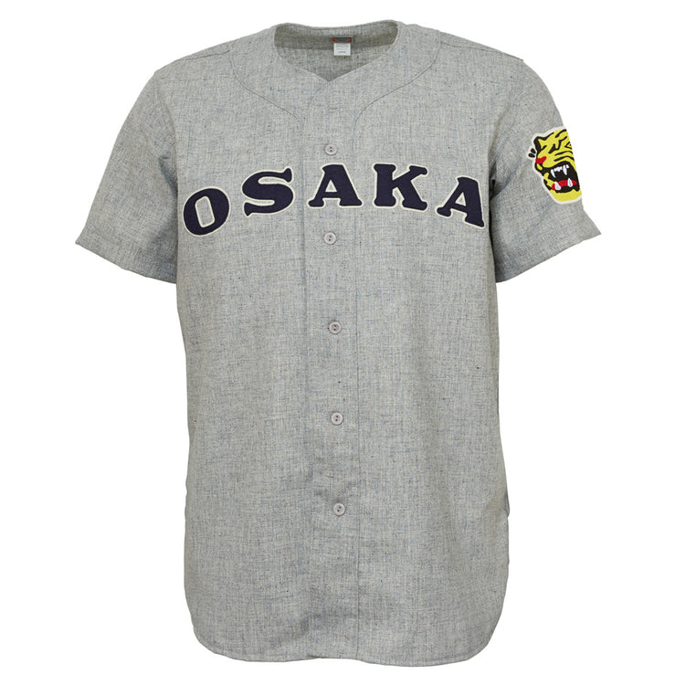 The EFF Osaka Tigers 1959 Road Jersey is a gray Japanese baseball jersey with OSAKA in bold black letters across the chest, a yellow tiger head patch on the left sleeve, button front, and short sleeves—classic Tigers inspiration.