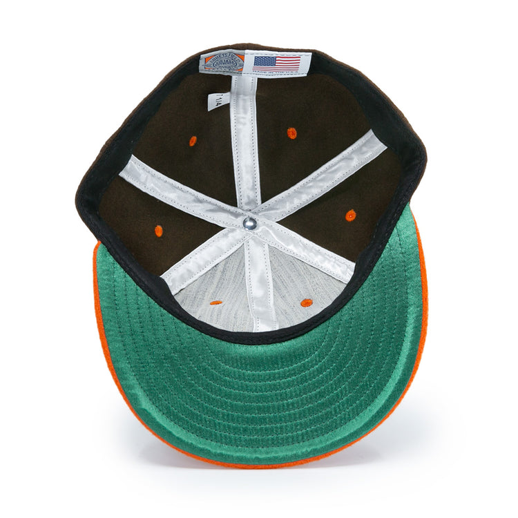 A top-down view of the Ebbets Field Flannels Satchel Paige 1952 Signature Series Ballcap in green and orange, showing inner stitching, a white sweatband, orange ventilation holes, and an American flag tag.