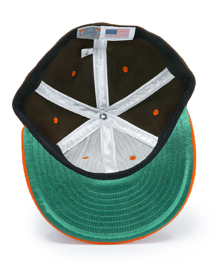 A top-down view of the Ebbets Field Flannels Satchel Paige 1952 Signature Series Ballcap in green and orange, showing inner stitching, a white sweatband, orange ventilation holes, and an American flag tag.