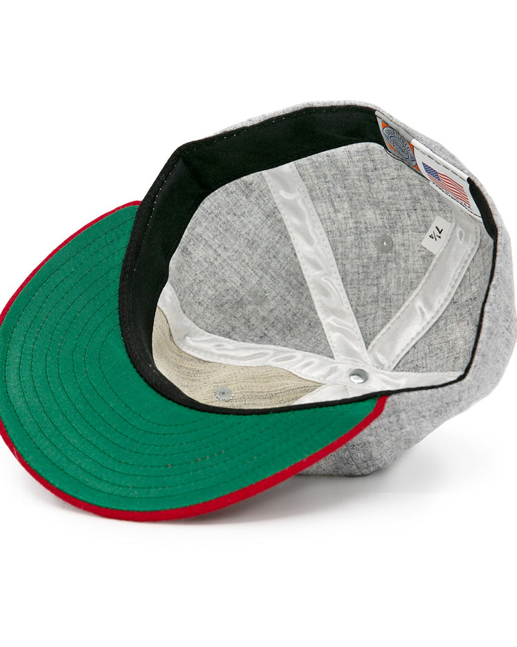 The Regina Nationals 1933 Vintage Ballcap by Ebbets Field Flannels is shown inside out, highlighting its green brim underside with a red edge, white inner lining, and visible tag.