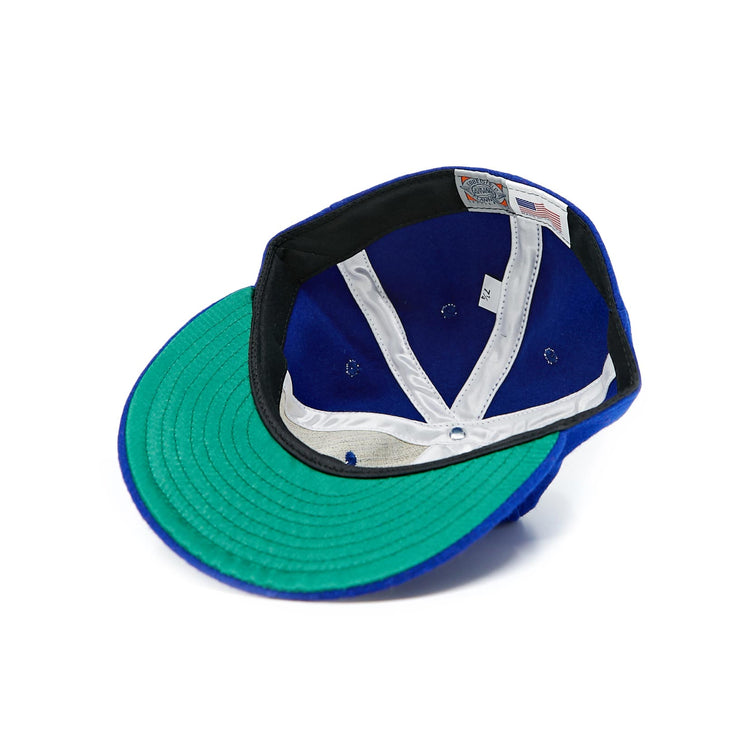 The EFF Seattle Rainiers 1941 Vintage Ballcap is shown upside down on a white background, highlighting its green underbrim, white sweatband, blue interior, and tags.