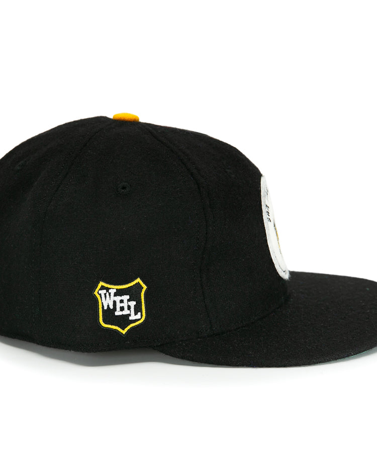 The EFF San Francisco Seals 1963 Vintage Ballcap is a black wool cap with a flat brim, yellow top button, yellow and white Western Hockey League shield logo on the side, and a partial round white patch on the front.