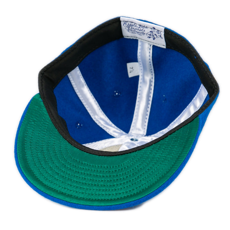 An EFF Southern Methodist University 1962 Vintage Ballcap in blue is shown upside down, displaying a green underbrim, black inner band, white satin lining, and an interior label with text and a lion graphic.