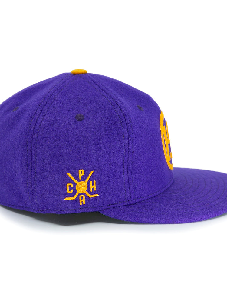 The EFF Spokane Canaries 1917 Vintage Ballcap is a purple wool cap with a yellow embroidered C P H A crossed bats logo, inspired by the Pacific Coast Hockey Association. It features an adjustable leather strap and a yellow top button.