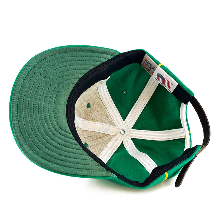 An overhead view of the St. Patrick Shamrocks 1925 Vintage Ballcap by EFF shows its green wool, black adjustable strap, white lining, visible stitching, a US flag tag, and a made in the USA label sewn near the back.