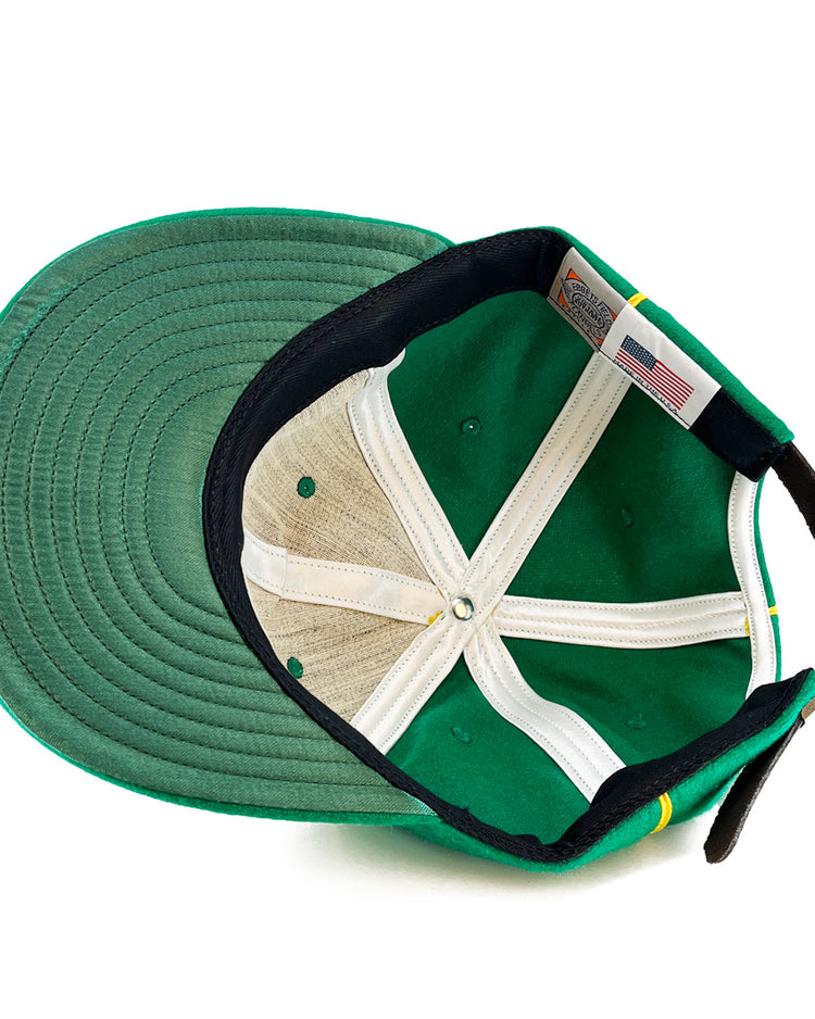 An overhead view of the St. Patrick Shamrocks 1925 Vintage Ballcap by EFF shows its green wool, black adjustable strap, white lining, visible stitching, a US flag tag, and a made in the USA label sewn near the back.