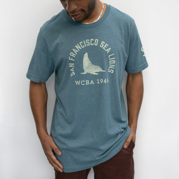 A man wears the EFF San Francisco Sea Lions 1946 T-Shirt, featuring a graphic sea lion and San Francisco Sea Lions WCBA 1946, celebrating the West Coast Baseball Association, against a plain white background.