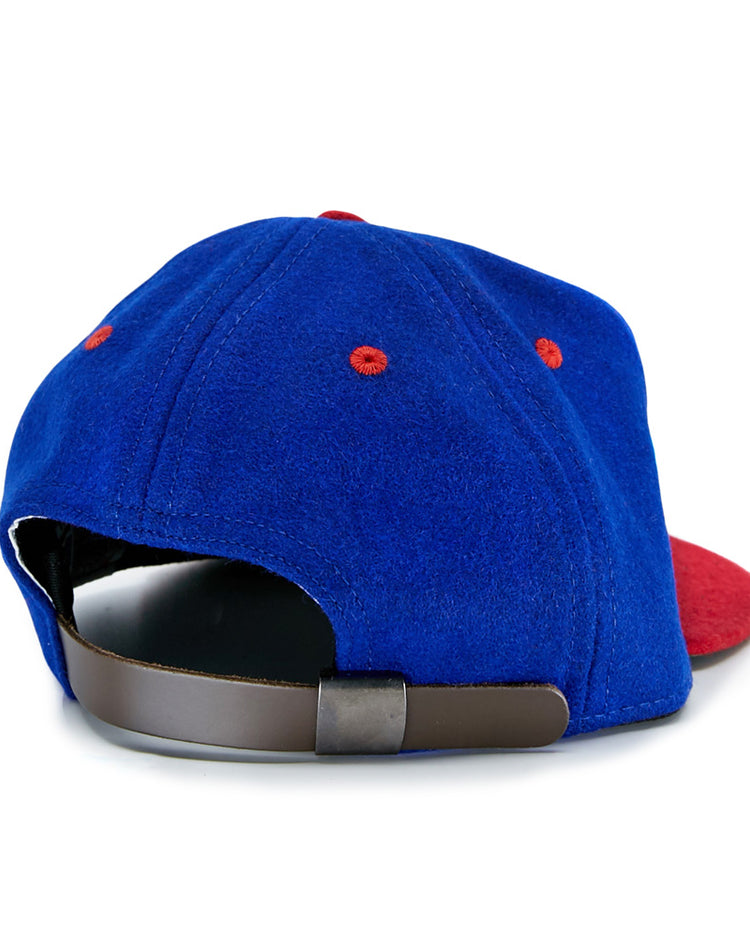 The EFF Utica Blue Sox 1950 Vintage Ballcap is a blue cap with red accents, seen from the back, featuring a brown adjustable strap and a partially visible red brim—capturing classic team style.