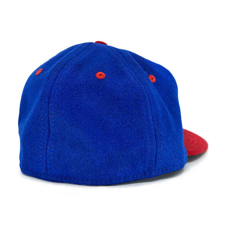 The EFF Utica Blue Sox 1950 Vintage Ballcap is a blue wool hat with red ventilation eyelets and a red curved brim, displayed from the back.