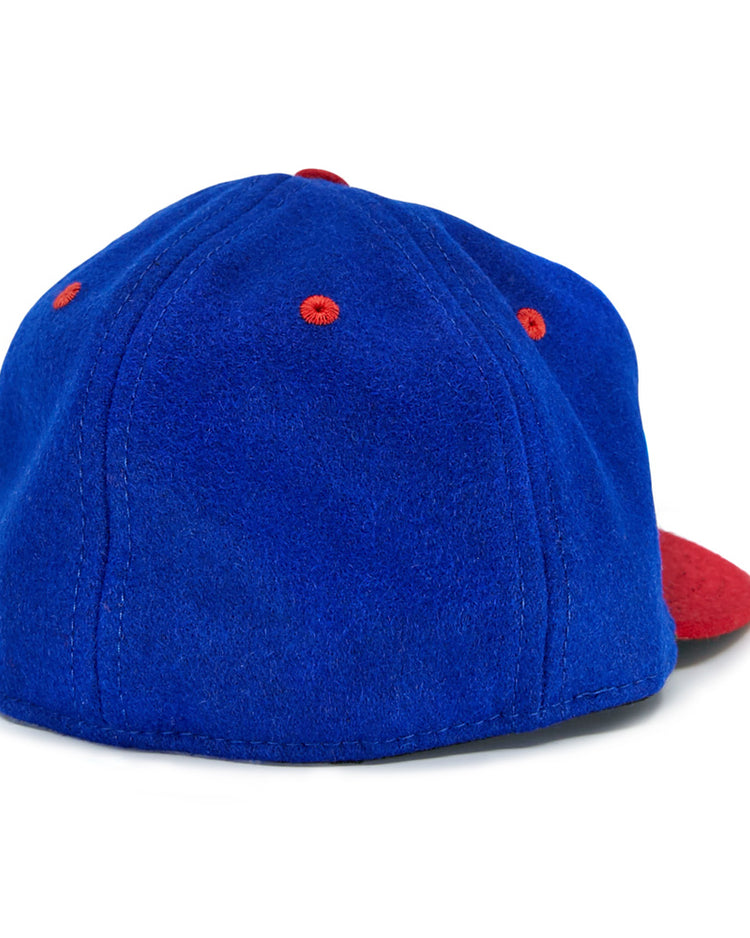The EFF Utica Blue Sox 1950 Vintage Ballcap is a blue wool hat with red ventilation eyelets and a red curved brim, displayed from the back.