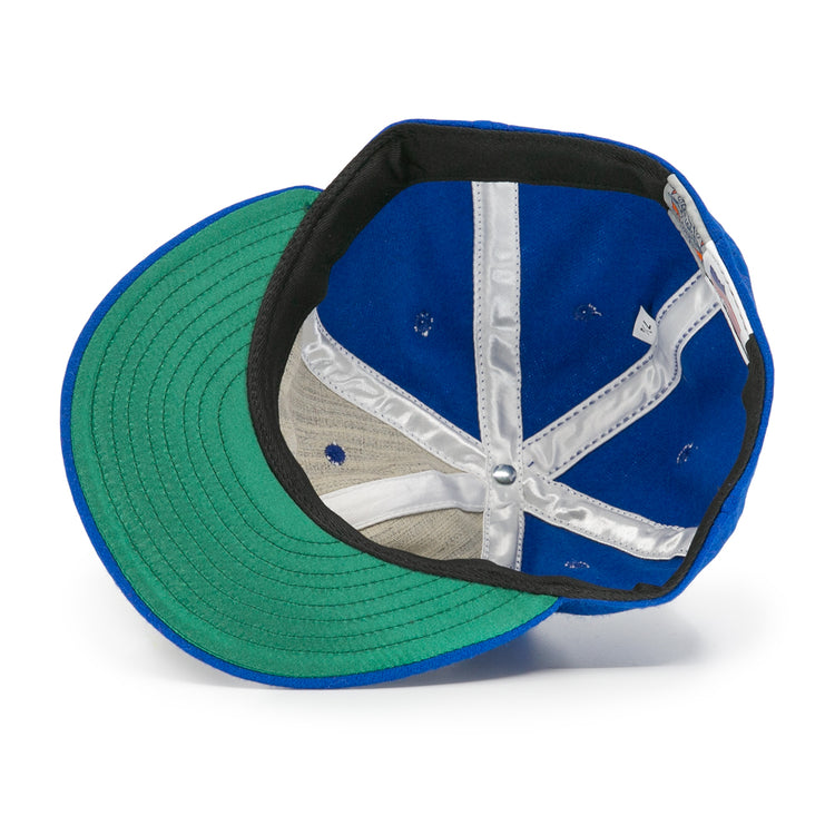 The image shows the inside of an EFF Wichita Falls Spudders 1956 Vintage Ballcap, featuring a blue wool exterior, green brim underside, silver inner seam lining, and a white tag on the inner band.