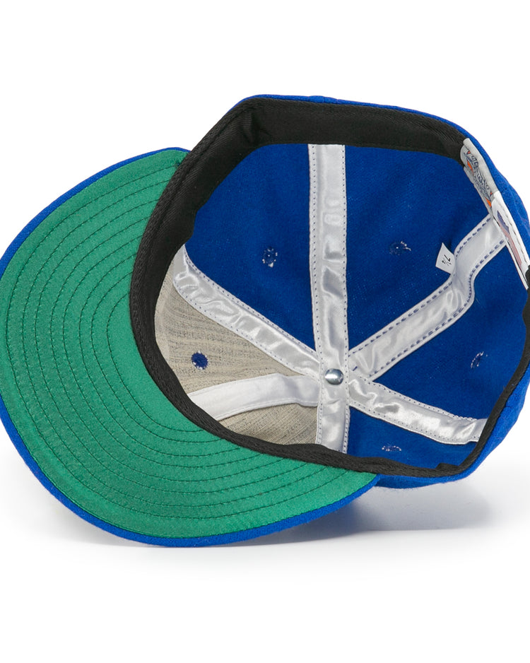 The image shows the inside of an EFF Wichita Falls Spudders 1956 Vintage Ballcap, featuring a blue wool exterior, green brim underside, silver inner seam lining, and a white tag on the inner band.