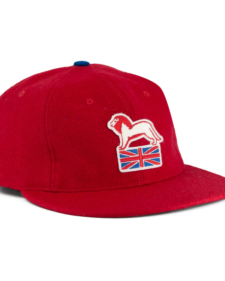 The EFF Wembley Lions 1957 Vintage Ballcap is a red wool cap with an embroidered white lion on a Union Jack, blue top button, and flat brim—reflecting classic British National Hockey League style.