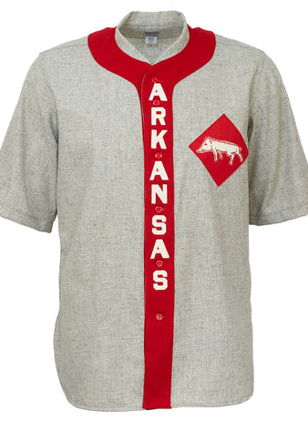 The EFF University of Arkansas 1912 Road Jersey is a gray, short-sleeve college baseball shirt with a red vertical stripe reading ARKANSAS in white and a red diamond patch featuring a white razorback logo—an authentic vintage reproduction.